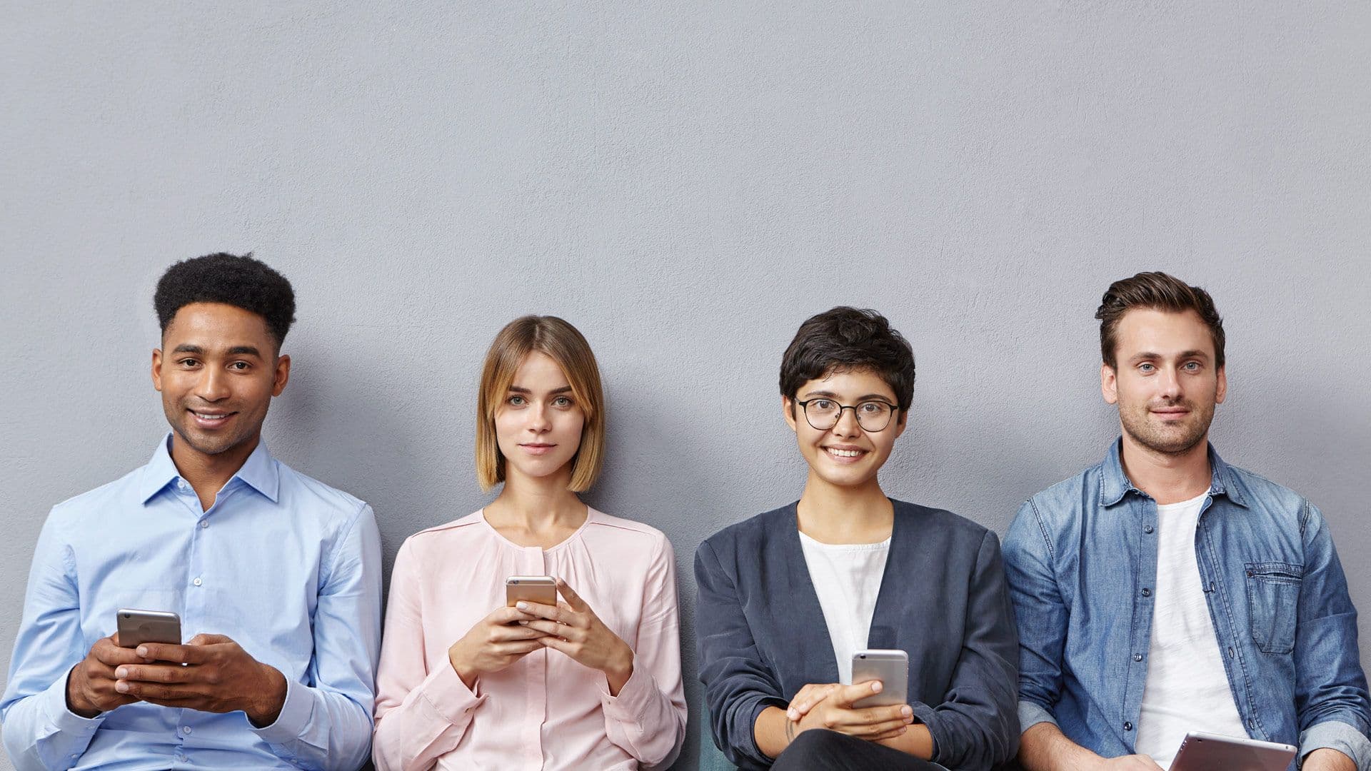 a group of people are sitting next to each other looking at their phones .